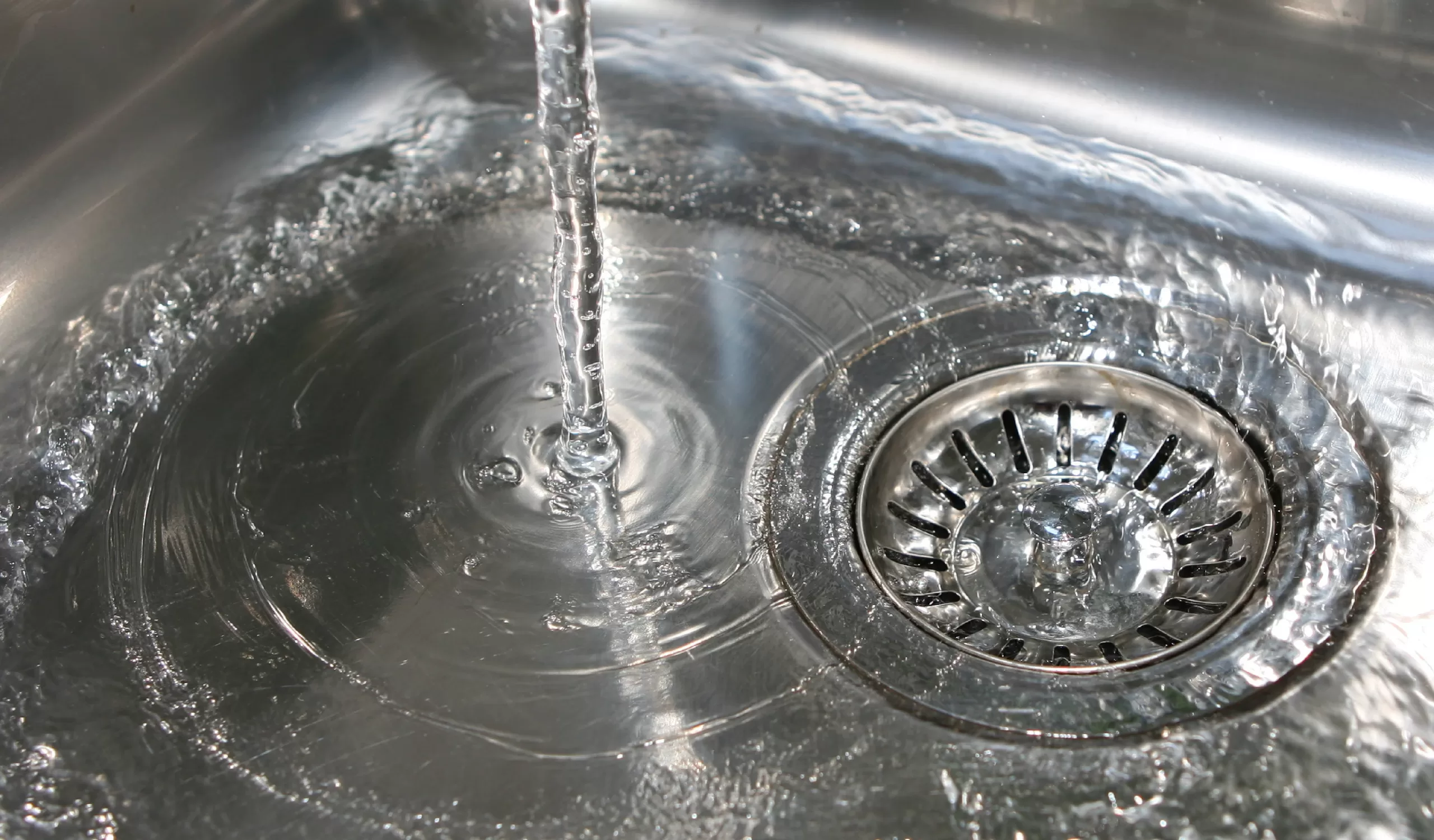 hot water runs from a kitchen faucet into a stainless steel sink to check the drain flow