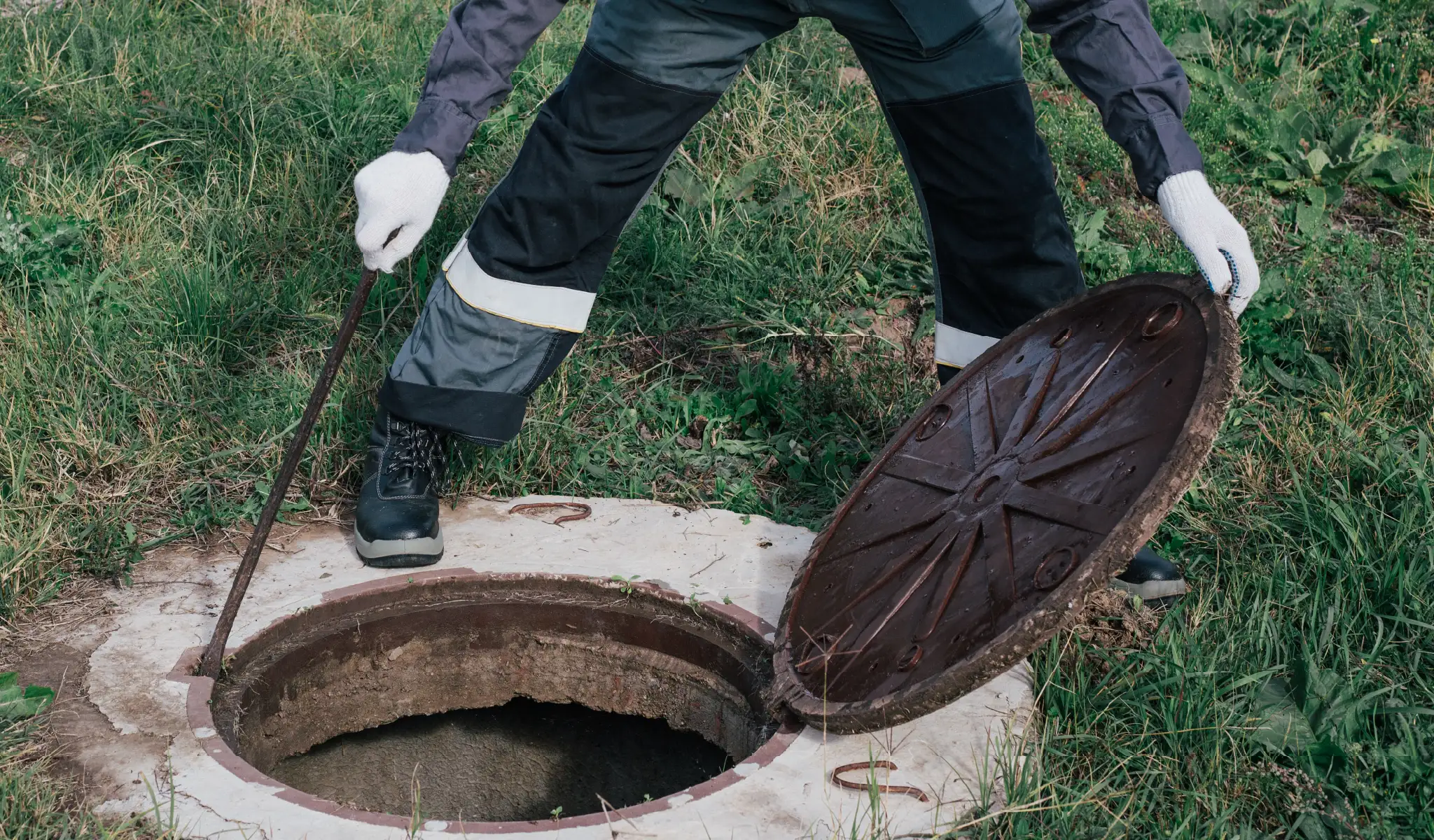Worker opens septic well manhole cover for septic tank maintenance.